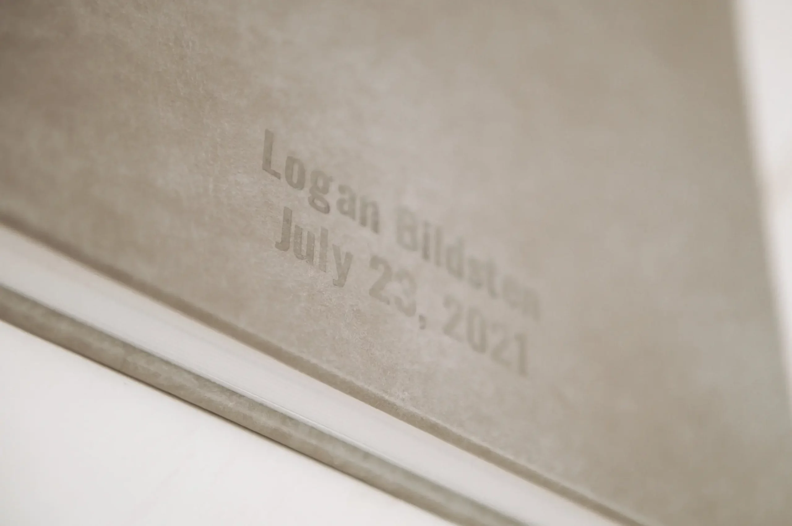 Close-up of a beige book cover with embossed text that reads "Logan Bildsten July 23, 2021