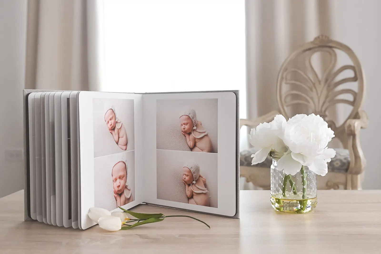 An open photo album on a wooden table displays four pictures of a sleeping newborn