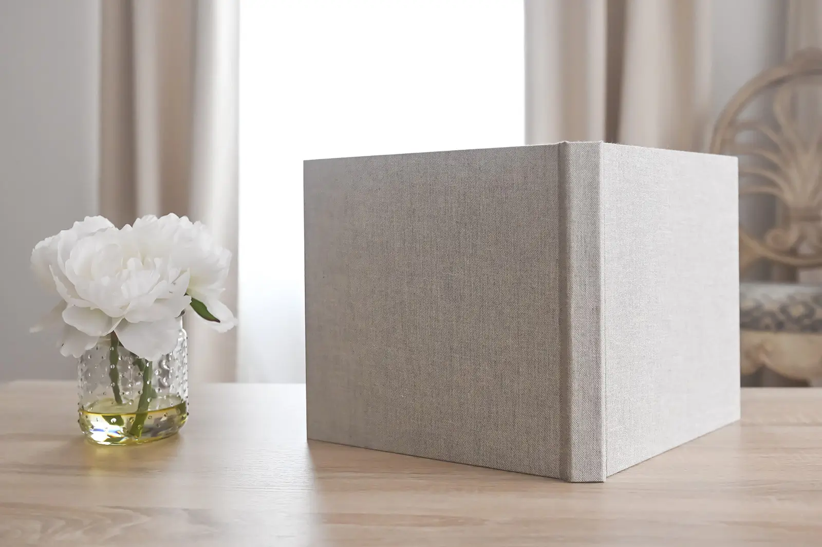 Linen-covered heirloom photo album on a wooden table next to white peonies